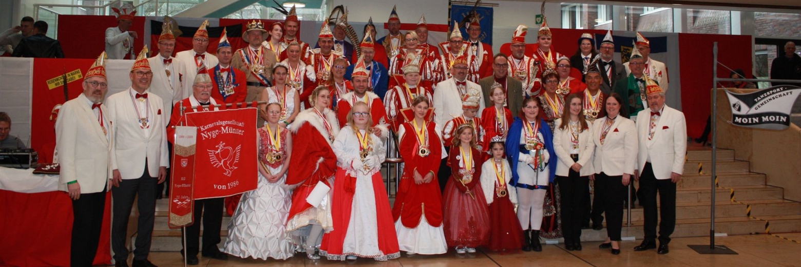 Eine große Gruppe von Menschen in traditionellen und festlichen Gewändern posiert in einer hellen, modernen Veranstaltungshalle.